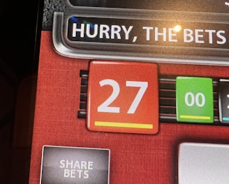 A digital display screen showing a casino betting interface, with text prompting to hurry bets and a highlighted number 27 in red. There are options for betting amounts and a 'share bets' button.
